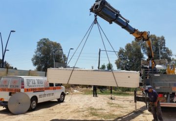 יחידת בטון לאחר ניסור תלויה על מנוף לצד רכב עבודה של החברה